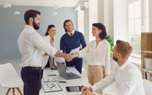 man shaking woman's hand surrounded by smiling coworkers